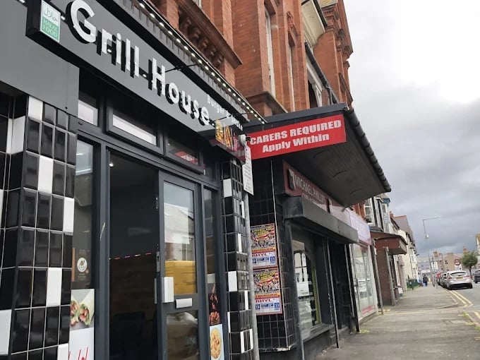 Street view of storefronts with a closed business displaying staff required apply within sign on brick building