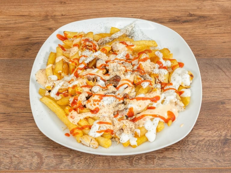 Loaded french fries on a white plate topped with cheese sauce, sriracha drizzle, and herbs on a wooden surface