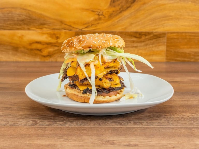 Gourmet burger with melted cheese, corn, shredded cabbage on white plate against wooden background