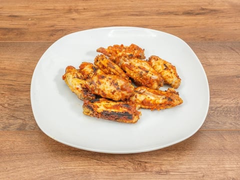 Golden-brown grilled chicken strips with char marks on a white plate over a wooden surface