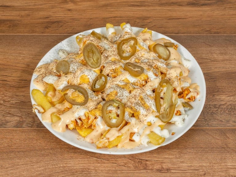 Loaded French fries topped with powdered sugar, cheese, and sliced jalapeños on a white plate