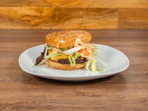 Gourmet cheeseburger with sesame seed bun, melted cheese, and fresh lettuce on white plate