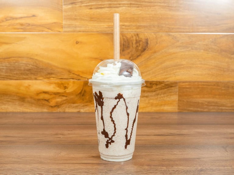 Iced coffee drink with whipped cream and chocolate drizzle in a plastic cup with straw on wooden table