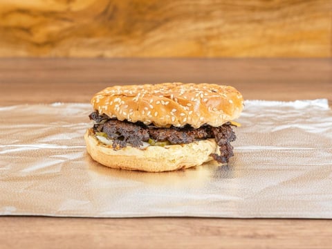 Gourmet burger with sesame seed bun and meat patty on parchment paper against wooden background